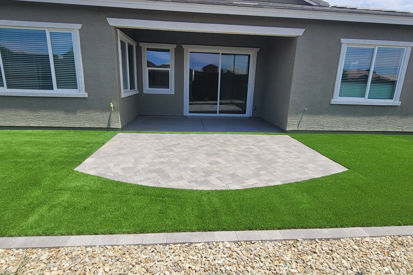 A paver patio beside the house, edged with artificial turf