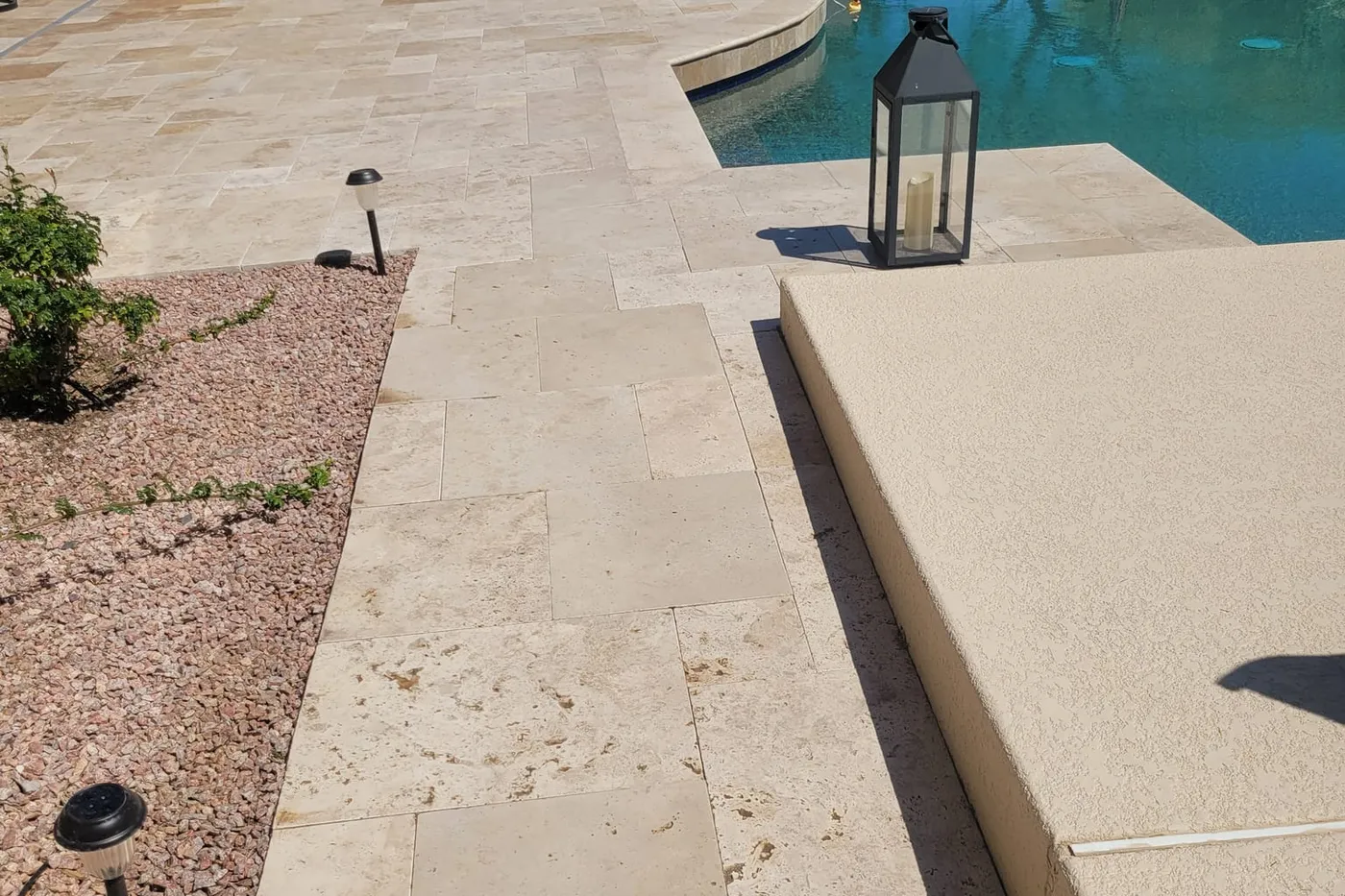 A travertine pool deck with a lantern at the water's edge